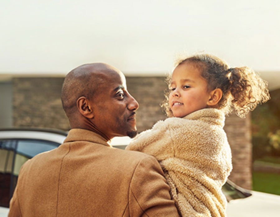 A man holds his young daughter in front of a parked BMW