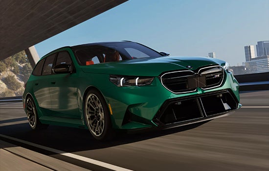 Green BMW M5 Touring driving on a city road. | BMW of Westbrook in Westbrook ME