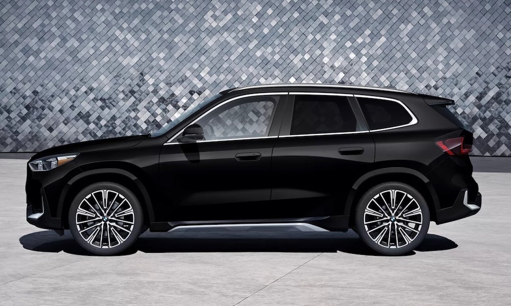 A black 2026 BMW X1 SUV parked in front of a tiled gray wall