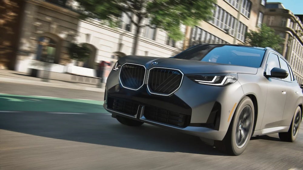 A gray 2026 BMW X3 driving down a city street
